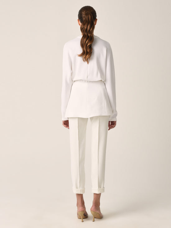 A white belted blazer with long sleeves, two front pockets, and a V-neck collar photographed against a plain background exudes modern elegance. This seasonless sleek white viscose piece, known as the Vogogna Jacket White, is a timeless addition to any wardrobe.