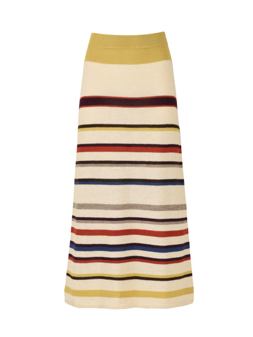 A person models the Brie Skirt Multi Mustard Stripe, featuring an off-the-shoulder design with long sleeves and ankle-length cut. Crafted from 100% baby alpaca and sustainably dyed, this striped knit piece is a standout choice that pairs perfectly with strappy sandals.