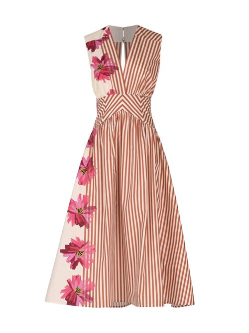 A woman is stylishly dressed in the Jocelyn Dress in Magenta Floral Brushstroke Stripes, featuring vertical orange accents, and paired with open-toed shoes for a charming daytime ensemble.