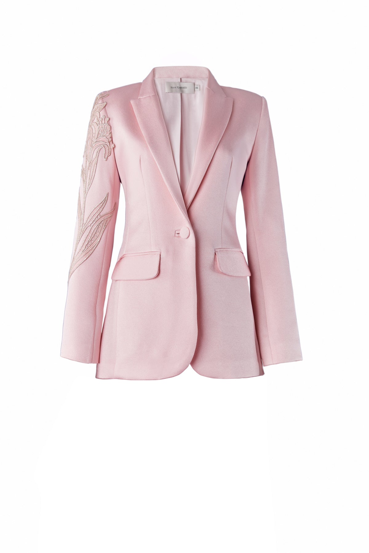 Profile view of a person with long hair tied back, wearing the Rebeca Jacket Pink, a light pink blazer adorned with intricate embroidery on the shoulder; pre-order now for delivery by February 1st, 2025.