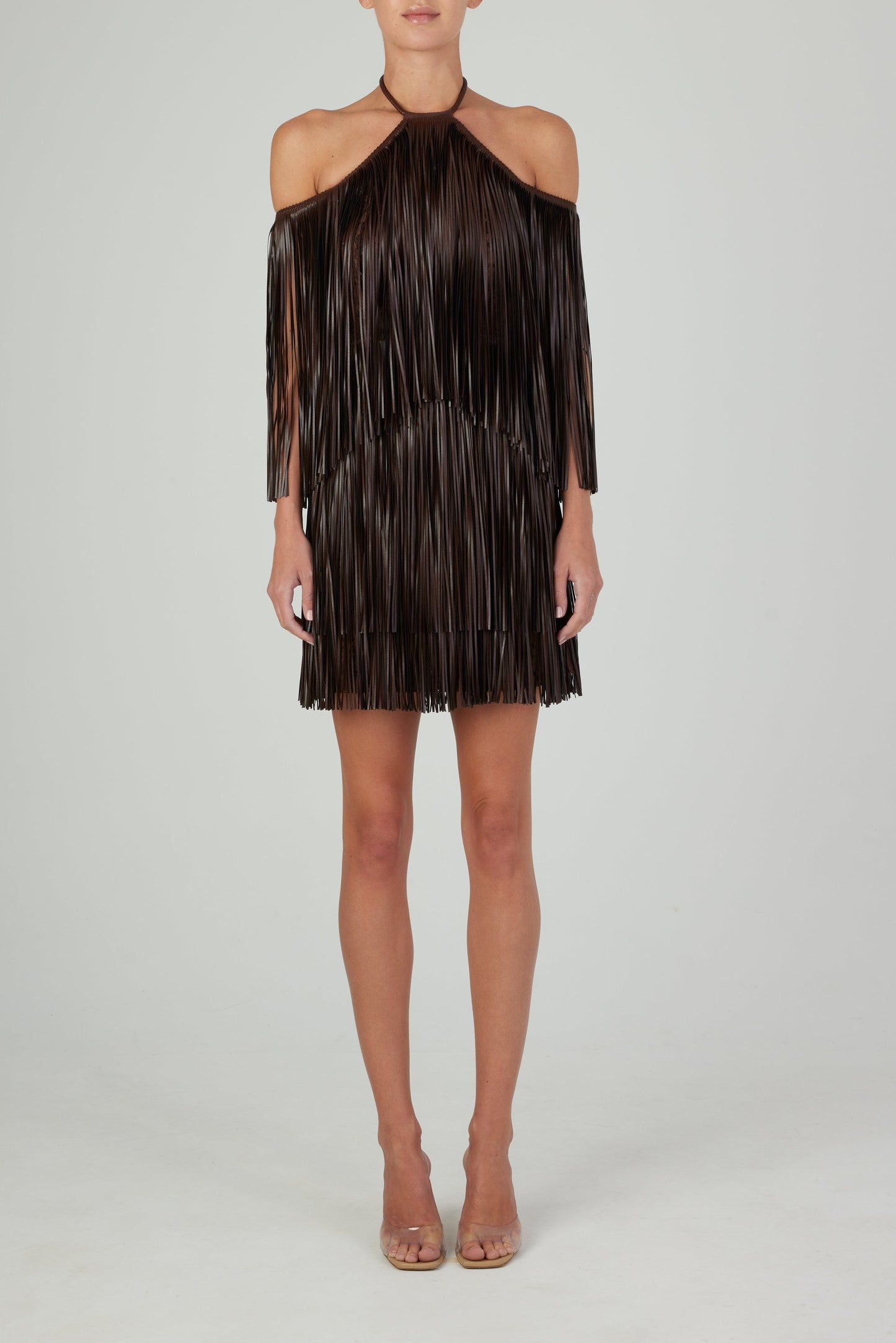 The Vercelli Dress Brown, featuring leather-like fringe and a deep chocolate hue, is displayed on a hanger against a plain white background.