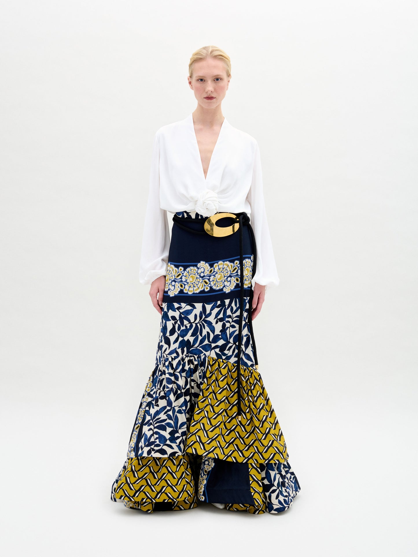 A model wears a white blouse paired with the Elliot Skirt, featuring a long design with a mix of blue, white, and yellow patterns.