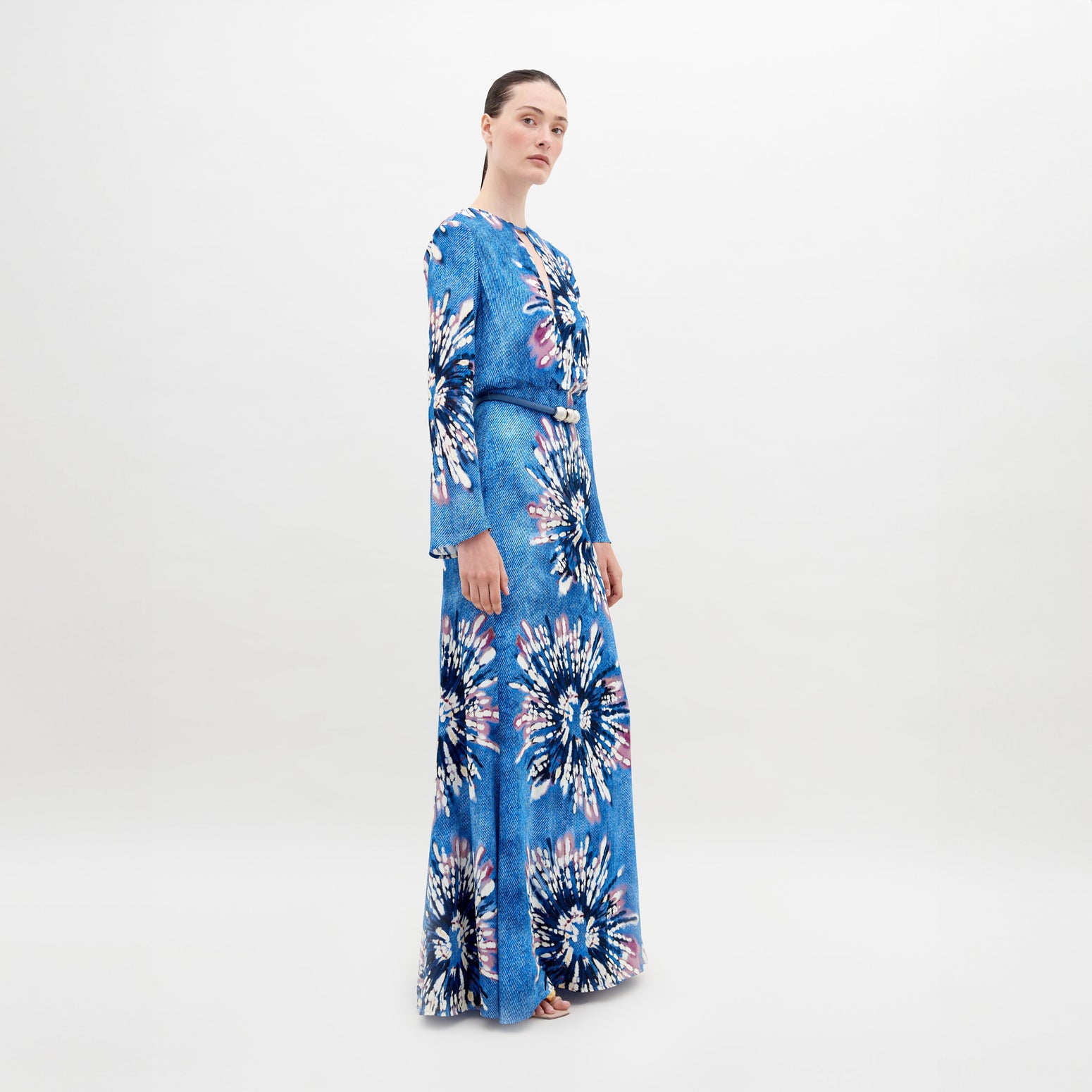 A person stands wearing the Ravenna Dress Aciano Flower, looking off to the side against a plain white background. Pre-order now to ensure it arrives by November 15th, 2024.