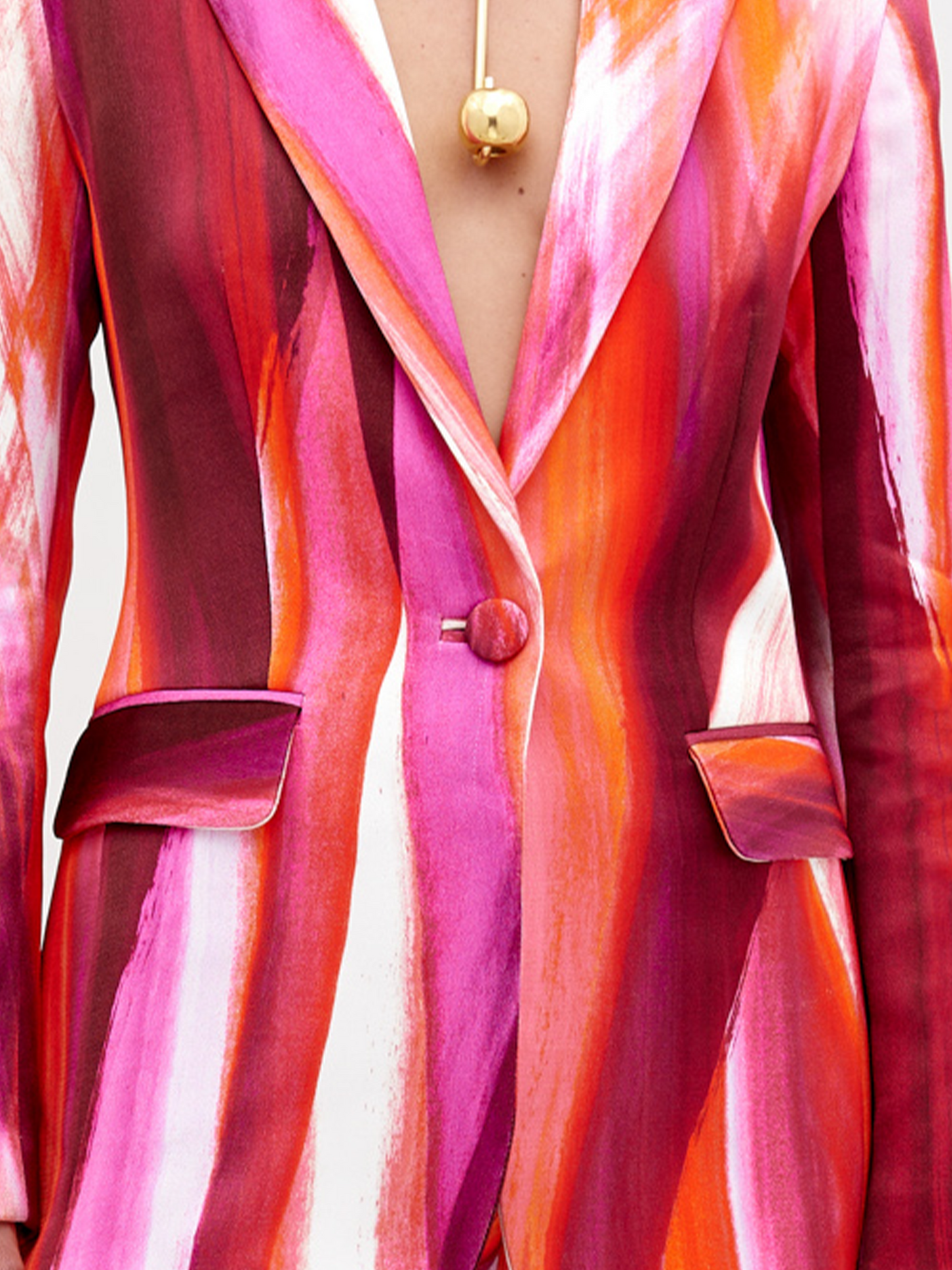 Woman wearing a vibrant, multi-colored striped Rebeca Jacket Magenta Abstract Waves with a deep neckline, accessorized with a chunky gold choker necklace, standing against a plain white background. Pre-order now and have it ship by date of November 15th, 2024.