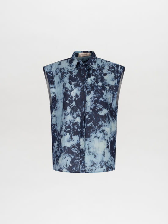 A woman wearing a blue tie-dye dress with a collar and sleeveless design, carrying a large navy blue bag on her shoulder, with her hair tied back in a ponytail, is showcasing the Rina Blouse Indigo exclusive pre-order item available until November 15th, 2024.