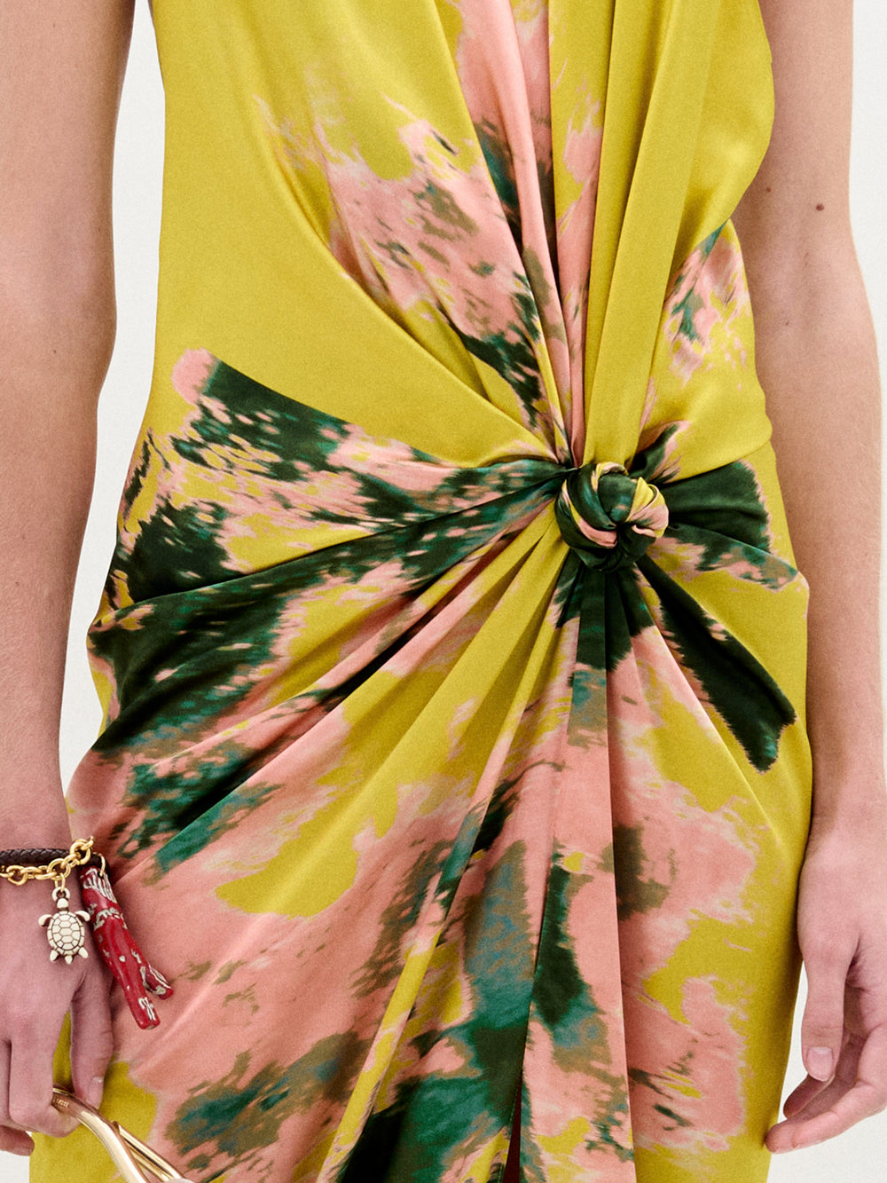 A person in the Sabrina Dress, a yellow and pink tie-dye style with a knotted front, holds a cream bag against a plain background.