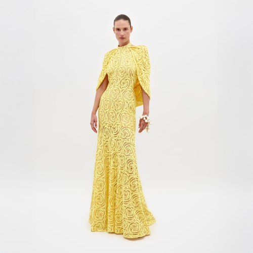 Person wearing a Salvina Dress Tuscany Yellow, adorned with a high neckline and cape-like sleeves, holding a pearl bracelet on their wrist, eagerly awaiting the pre-order ship date for 2025.