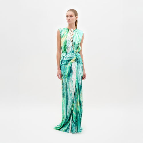 A person stands wearing the Samaira Dress Green Marble, a sleeveless, floor-length design featuring a striking green and white marble pattern. The outfit is completed with a high necklace adorned with large white beads, set against a plain white background. Pre-order now to ensure you receive yours by the February 15th, 2025 ship date.