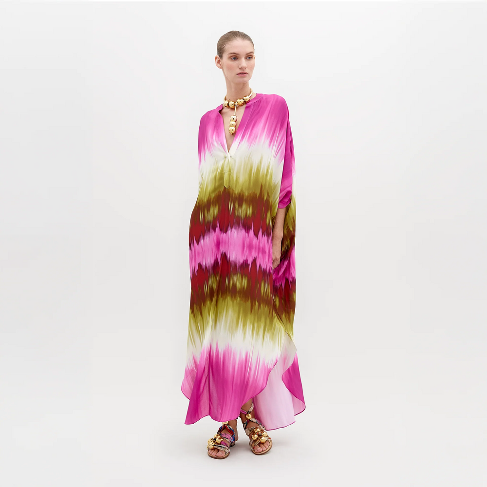 A person is wearing a colorful Serena Tunic Violeta Lime Tie Dye with shades of pink, green, and white. They are accessorized with a chunky gold necklace and sandals. The background is plain white. Get ready to pre-order this look by November 15th, 2024 to ensure you receive it by the ship-by date.