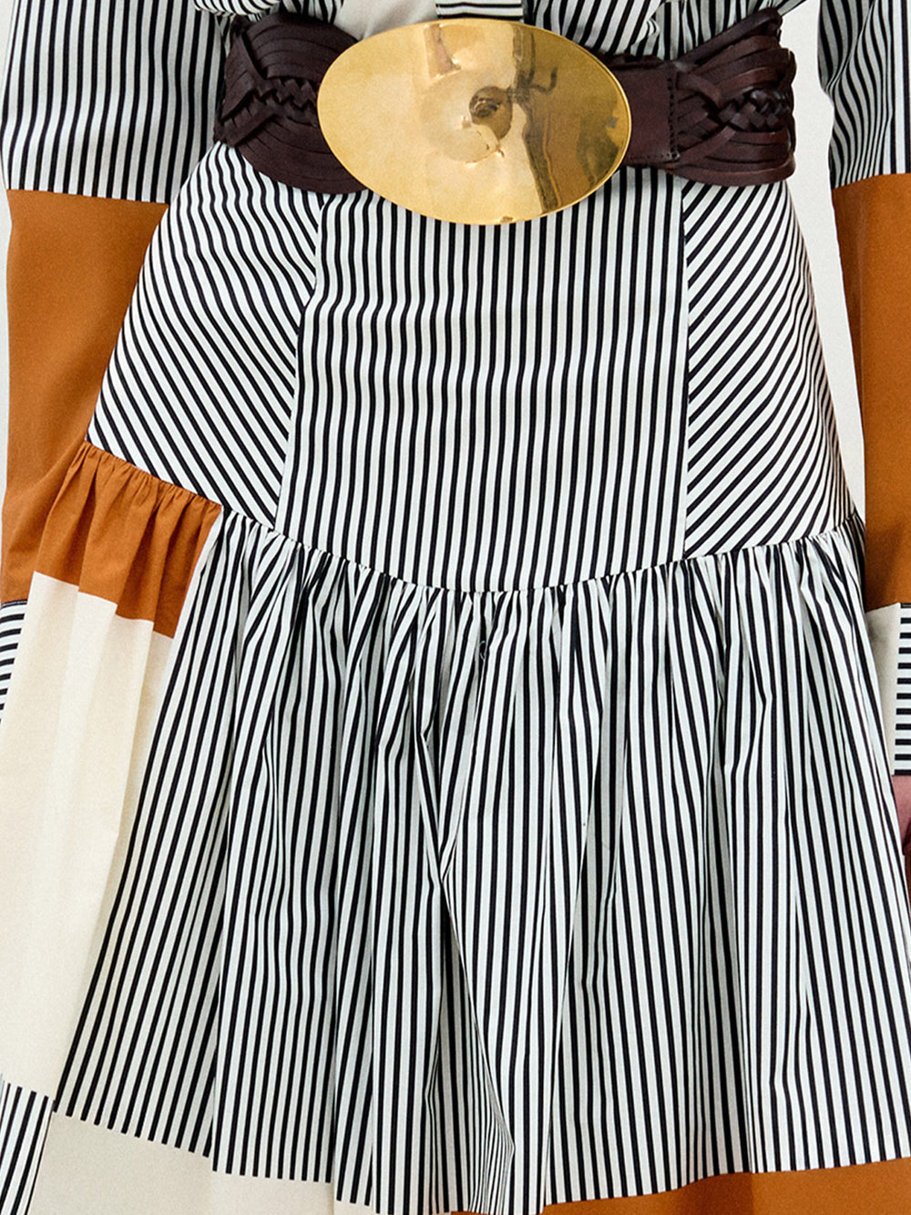 Black and white striped dress with a brown belt and gold buckle on a wooden surface.