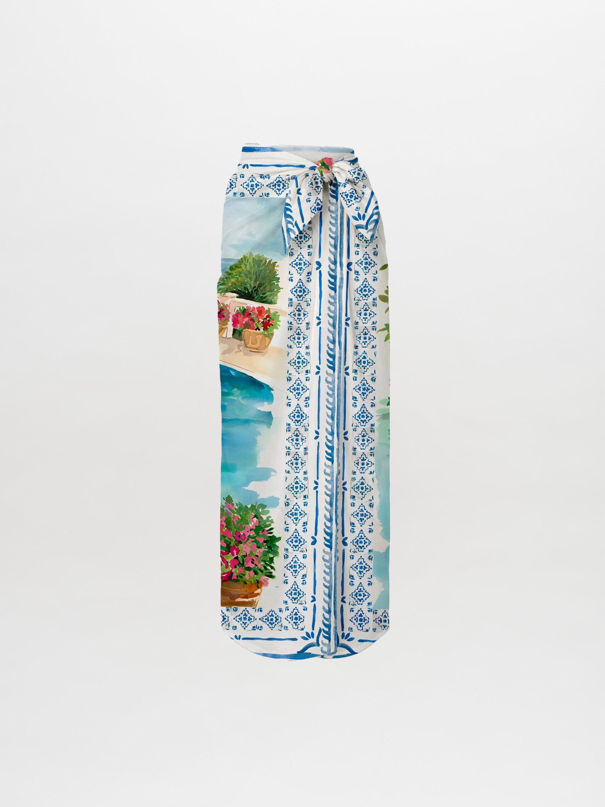 The La Isla Skirt Pareo is a long, high-waisted skirt with a blue and white geometric pattern and watercolor poolside scene, featuring potted flowers, greenery, a stone wall, and a matching waist tie belt.