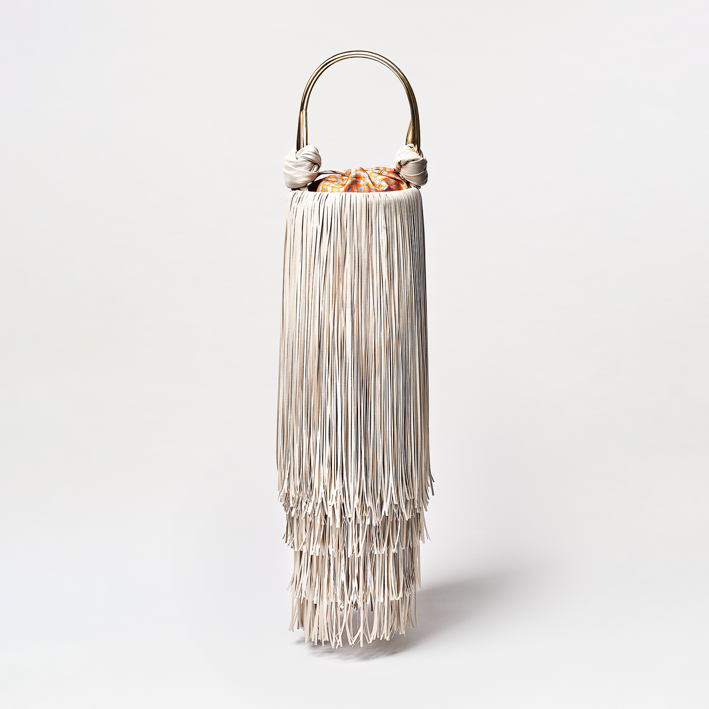 Cream fringe handbag with a metallic handle on a white background