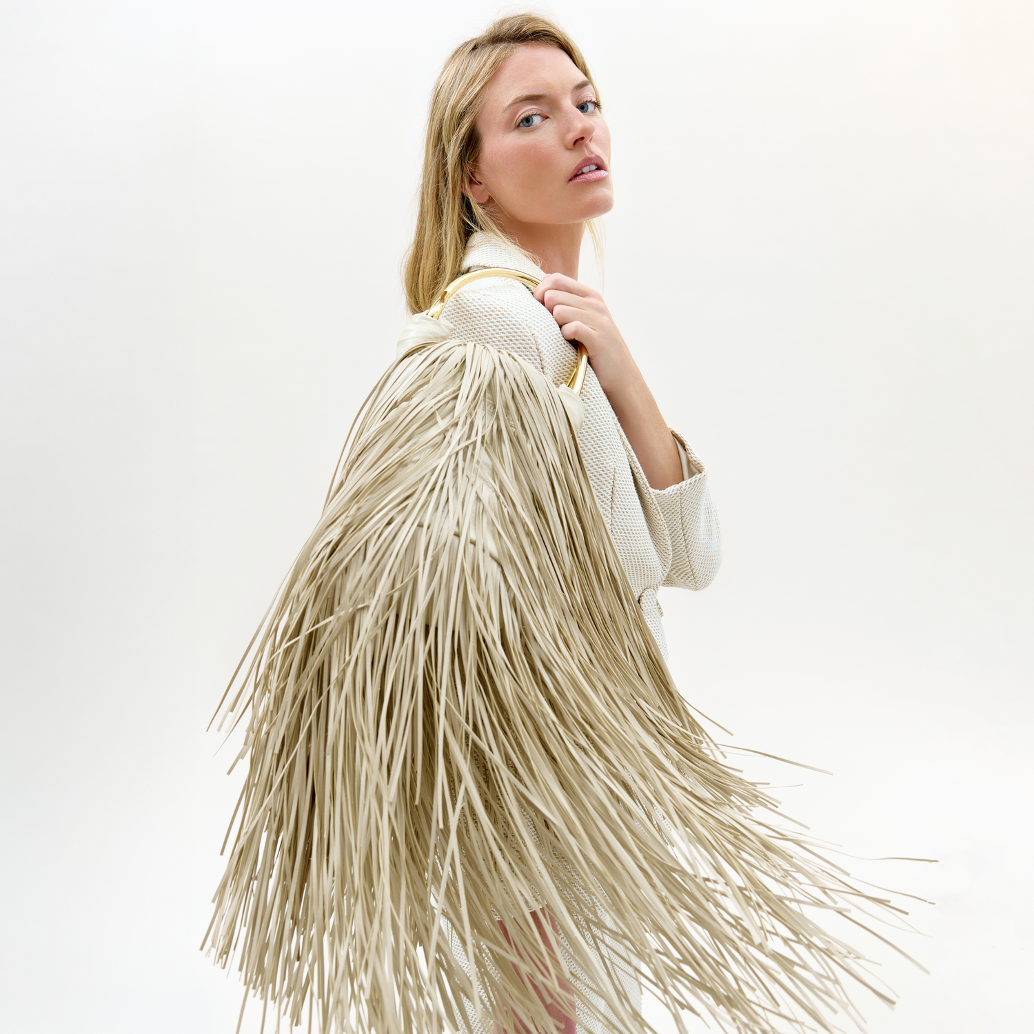 The supermodel Martha Hunt wearing a beige fringe jacket on a white background