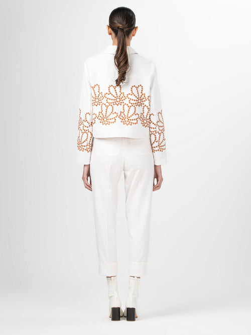 A Belen Jacket White Cacao Eyelet featuring a collared neckline and intricate brown beaded floral patterns on the front and sleeves, complemented by an effortlessly loose silhouette.