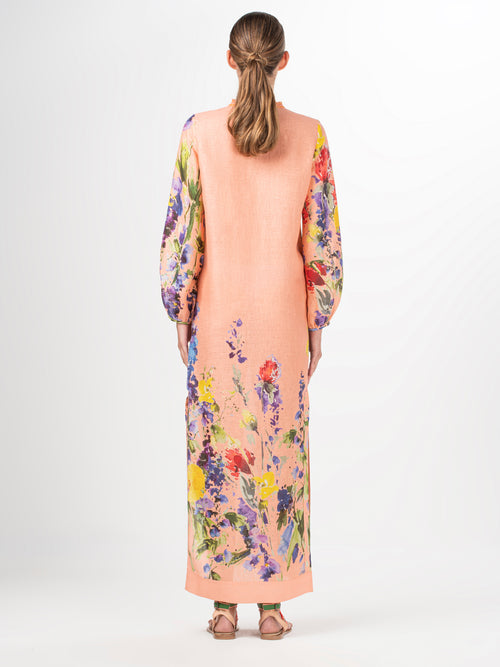 A long-sleeved, peach-colored Isernia Tunic Apricot Spring Garden with a floral pattern and fringe lace detailing on the chest. The tunic features vibrant flowers in various colors, including red, yellow, and purple.