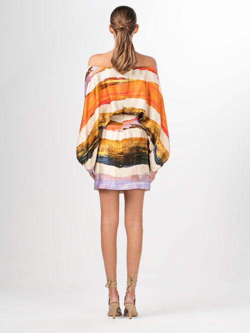 An off-the-shoulder Manon Dress Orange Orchid Abstract Stripes with an abstract painting.