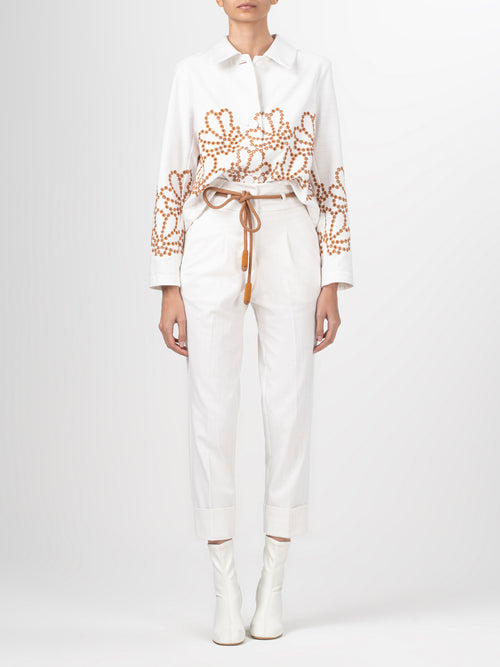 A Belen Jacket White Cacao Eyelet featuring a collared neckline and intricate brown beaded floral patterns on the front and sleeves, complemented by an effortlessly loose silhouette.