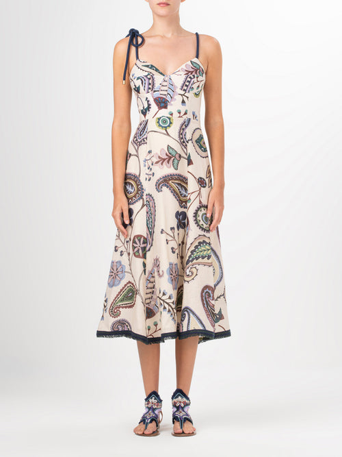 Introducing the Dalil Dress Blue Green Paisley: a sleeveless beige midi dress adorned with a vibrant floral and leaf pattern. It features a unique black tie strap on one shoulder and delicate fringe lace detailing, adding an elegant touch.