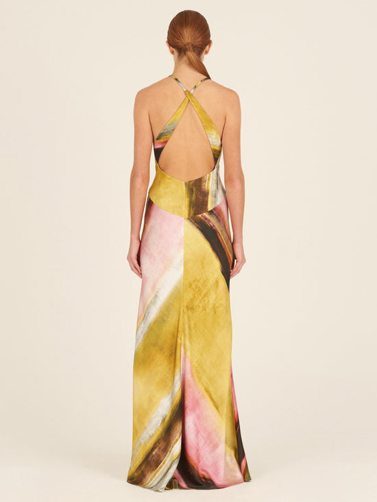 The Daniela Dress Canary Pink Stripes is a sleeveless, full-length piece crafted from crepe de silk, featuring a multicolor abstract pattern with canary pink stripes, a v-neckline, and crisscross straps at the back.