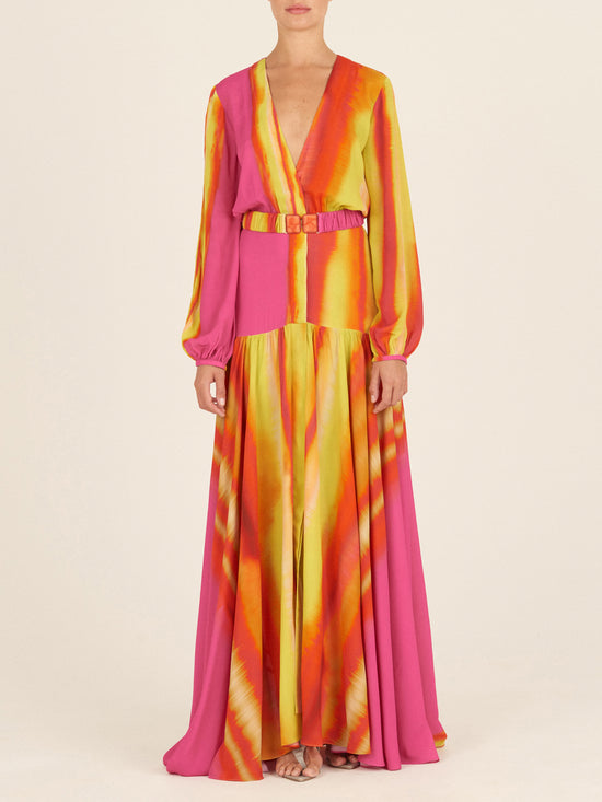 The Nagore Dress Fuschia Lime Stripes for Spring 2023 features a stunning V-neckline and long sleeves, crafted with a vibrant combination of bright pink, orange, and yellow tie-dye pattern accented by hints of fuschia and lime. Its cinched waist with a coordinating belt beautifully complements the flowing skirt.