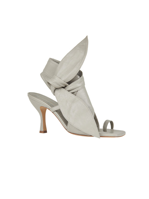 The Marco Heel Light Grey is an elegant high-heeled sandal featuring a fashionable open-toe design and a prominent bow accent, made from luxurious Italian calf leather in a light gray shade.