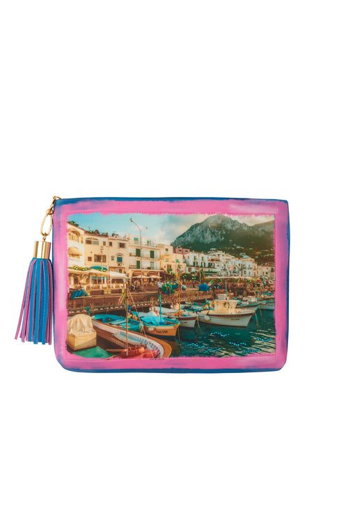 A Clutch Capri Barcos featuring an illustration of Capri's coastal harbor with boats and buildings in front of mountains, accented with a tassel zipper pull and adorned with sparkling Swarovski crystals.