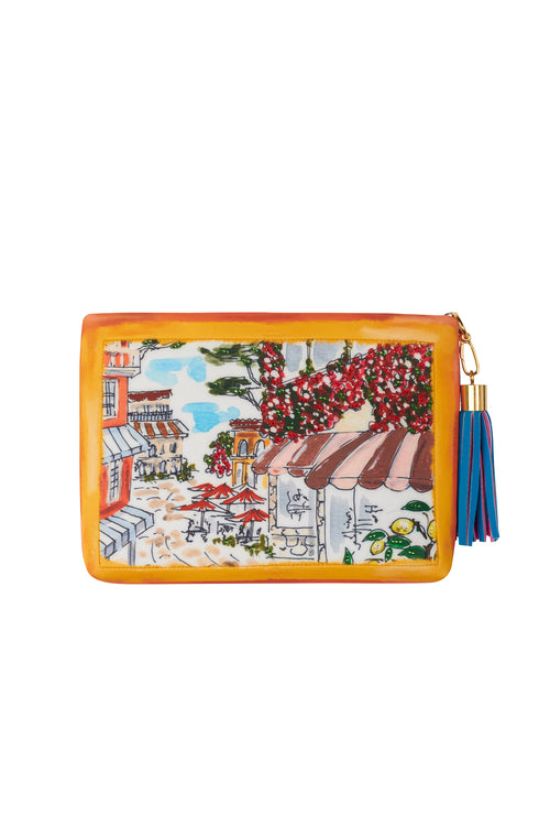 A Clutch Capri Barcos featuring an illustration of Capri's coastal harbor with boats and buildings in front of mountains, accented with a tassel zipper pull and adorned with sparkling Swarovski crystals.