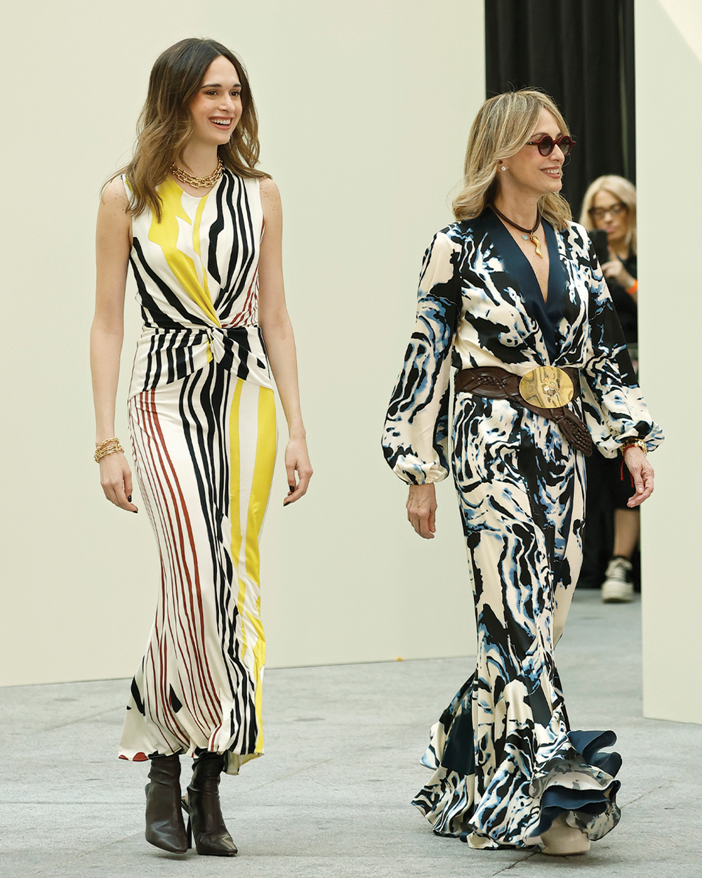 Two women walking on a catwalk wearing patterned outfits.