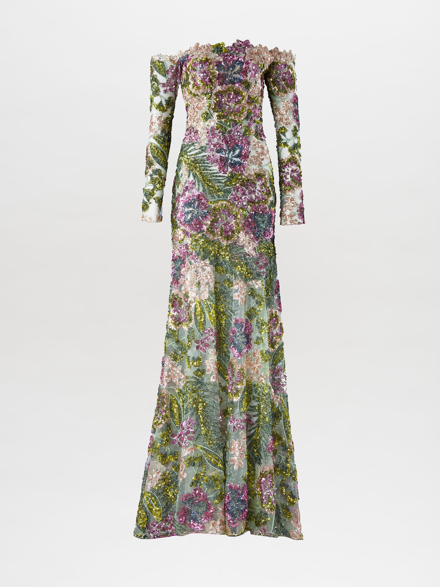 A person stands against a plain background wearing the Rafaella Dress Botanical Sequins, a floor-length, off-the-shoulder floral gown with long sleeves and adorned with a vibrant pattern of flowers and greenery. This elegant piece is available for pre-order now, with a ship-by date set for February 2025.