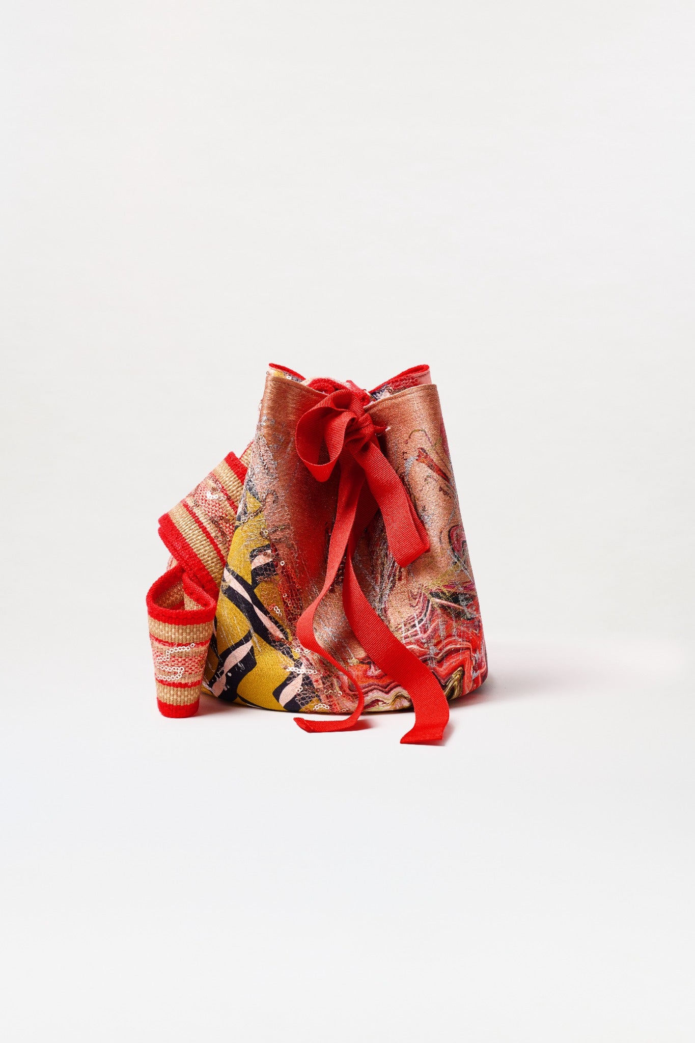 The Mochila Laaput Big is a large bag with bold red, yellow, and black abstract patterns, thick red fabric ties with a decorative bow, and a matching strap, shown against a plain white background.