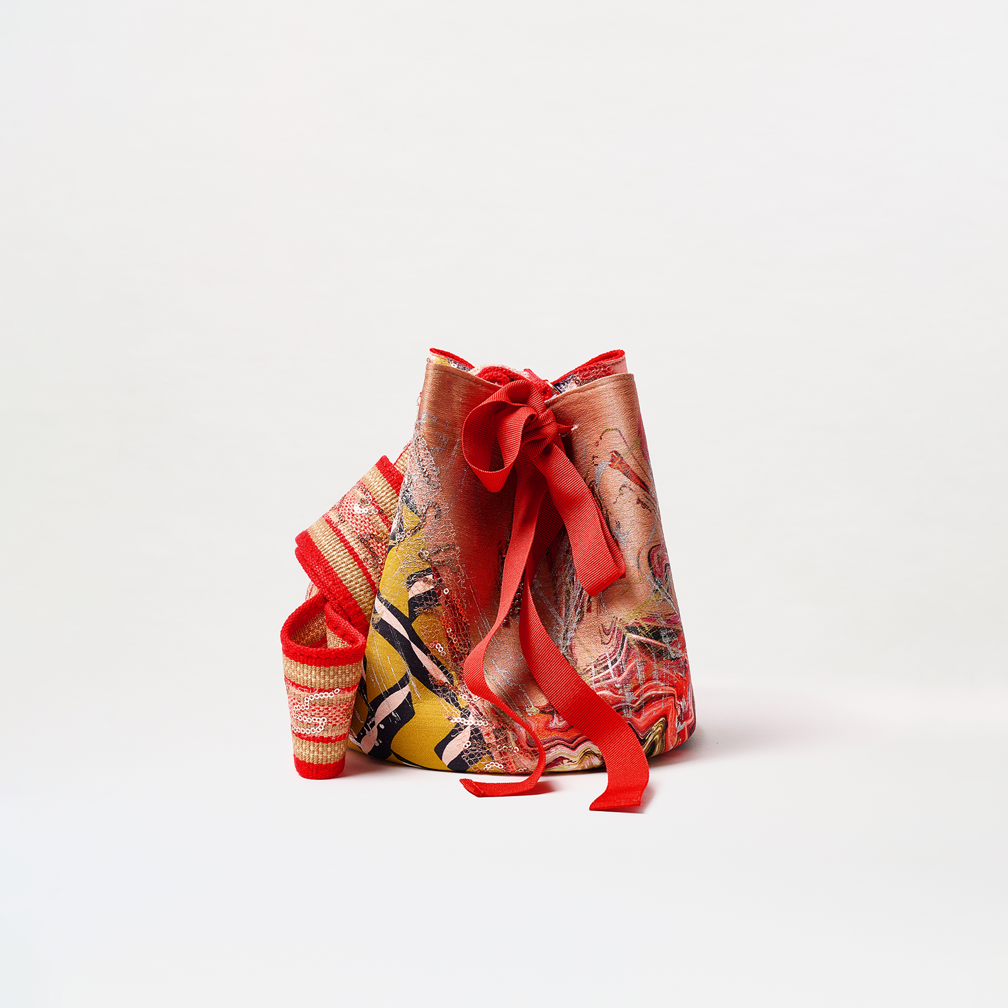 The Mochila Laaput Big is a large red bucket bag with an abstract red, yellow, and orange pattern, a decorative bow, and a wide woven red and cream strap, shown on a plain white background.