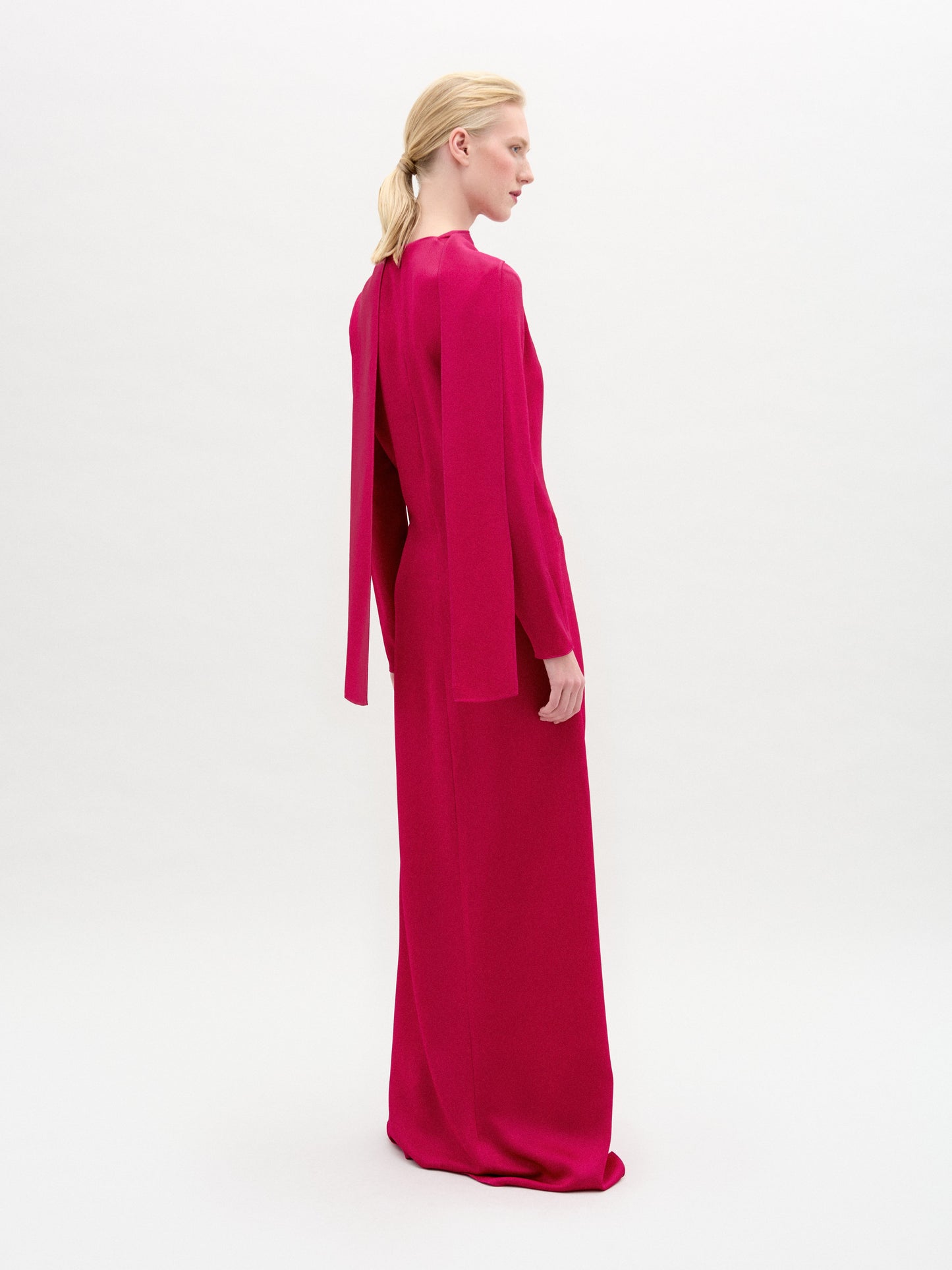 A person in the Sue Dress, a bright pink maxi with a keyhole neckline and front knot, stands against a plain white background.