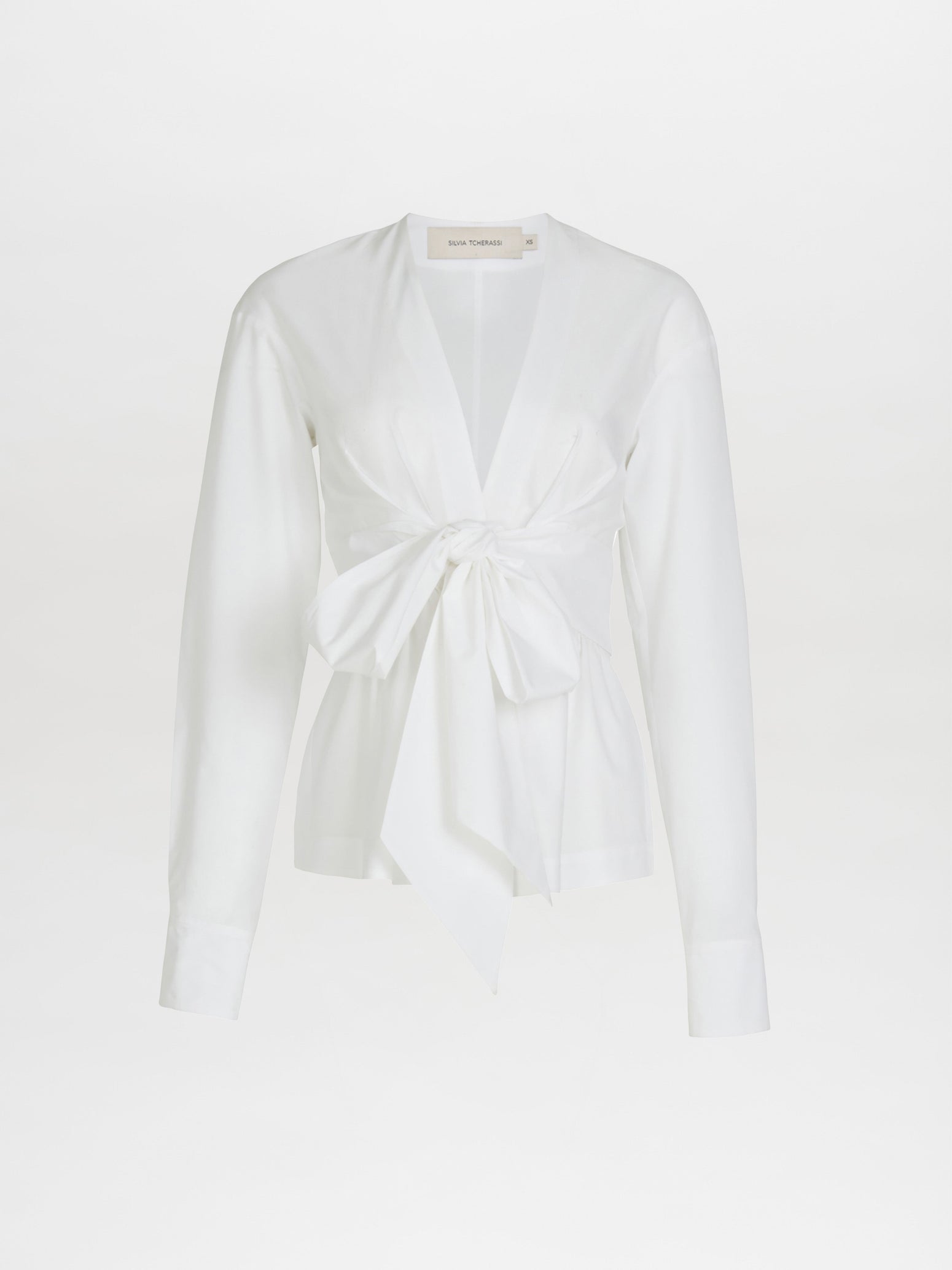 The Simona Blouse White showcases tailored sleeves and a deep V-neck, enhanced by a front tie knot for an elegant silhouette.