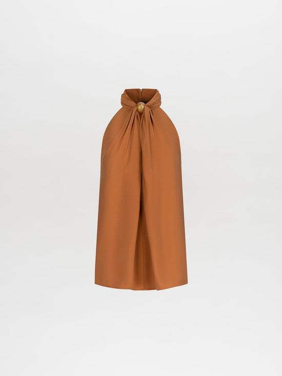 A person wearing the Shela Blouse Camel sleeveless high-neck top with matching wide-leg trousers, accessorized with a belt and holding a small object, stands against a plain white background. Pre-order now to ensure it ships by February 15th, 2025.