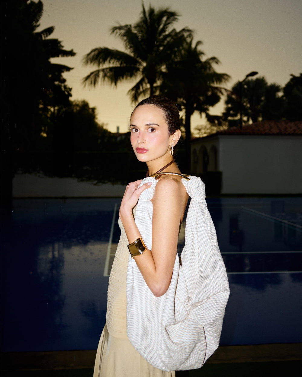 Woman holding a white bag by a pool with palm trees in the background