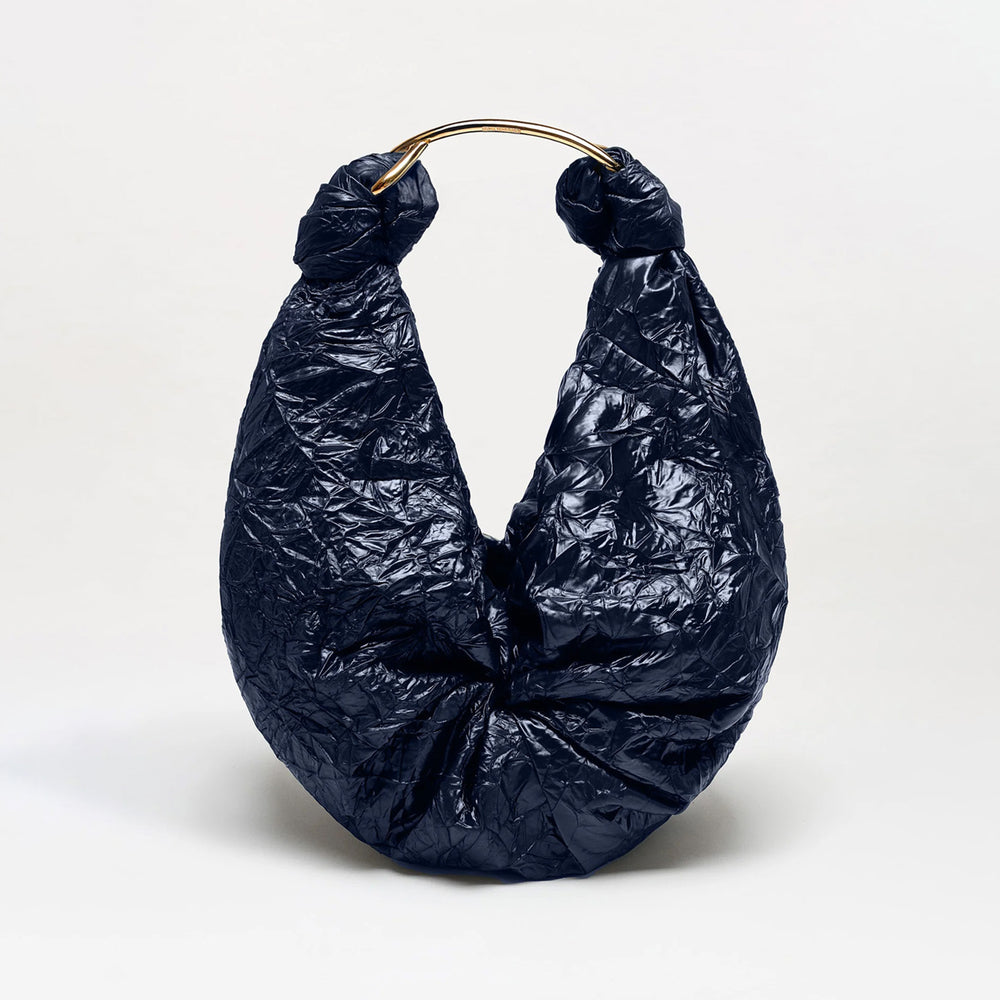 The Sofia Bag (Maxi) is a navy blue, crinkled handbag made from luxurious Italian fabric, featuring a crescent silhouette and a gold-toned handle, photographed against a plain white background.