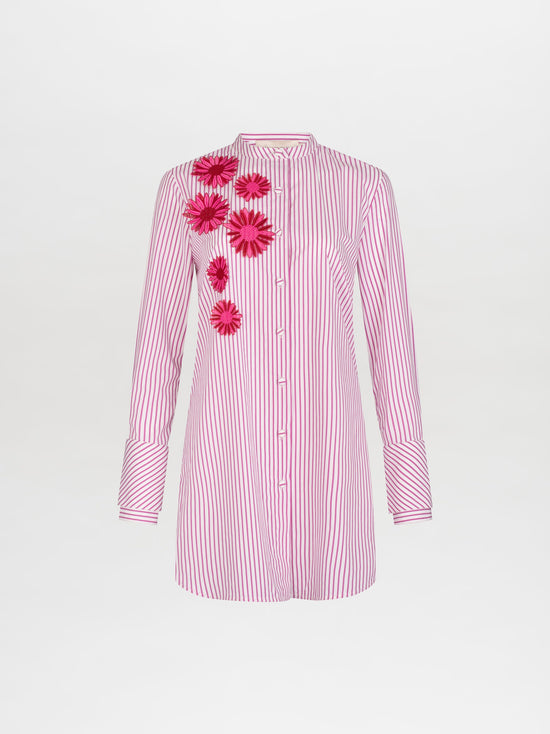 A person in the Silvina Blouse Rose Stripes adorned with floral appliqués, paired with a pink sequined skirt featuring similar floral designs, stands against a plain white background, available for pre-order now with an expected ship date in early 2025.