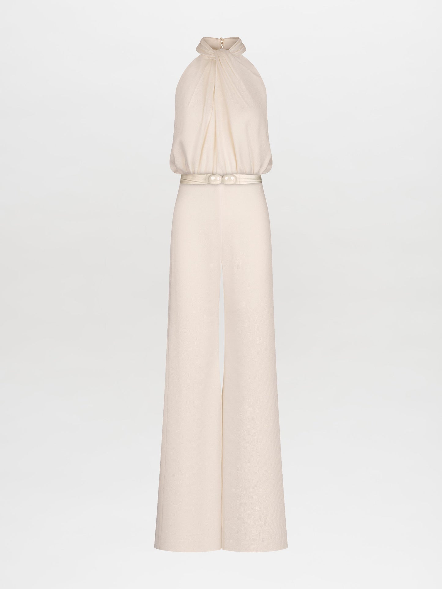 A woman stands against a plain background, wearing the Siv Jumpsuit White—a sleeveless halter jumpsuit featuring a beaded embellishment at the waist. This stunning piece is now available for pre-order and is set to ship by February 15th, 2025.