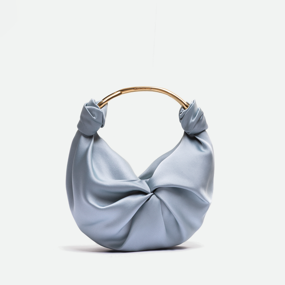 The Sofia Bag (Small) is a light blue silky handbag featuring a twisted knot design and a curved gold metal handle, displayed against a plain white background.