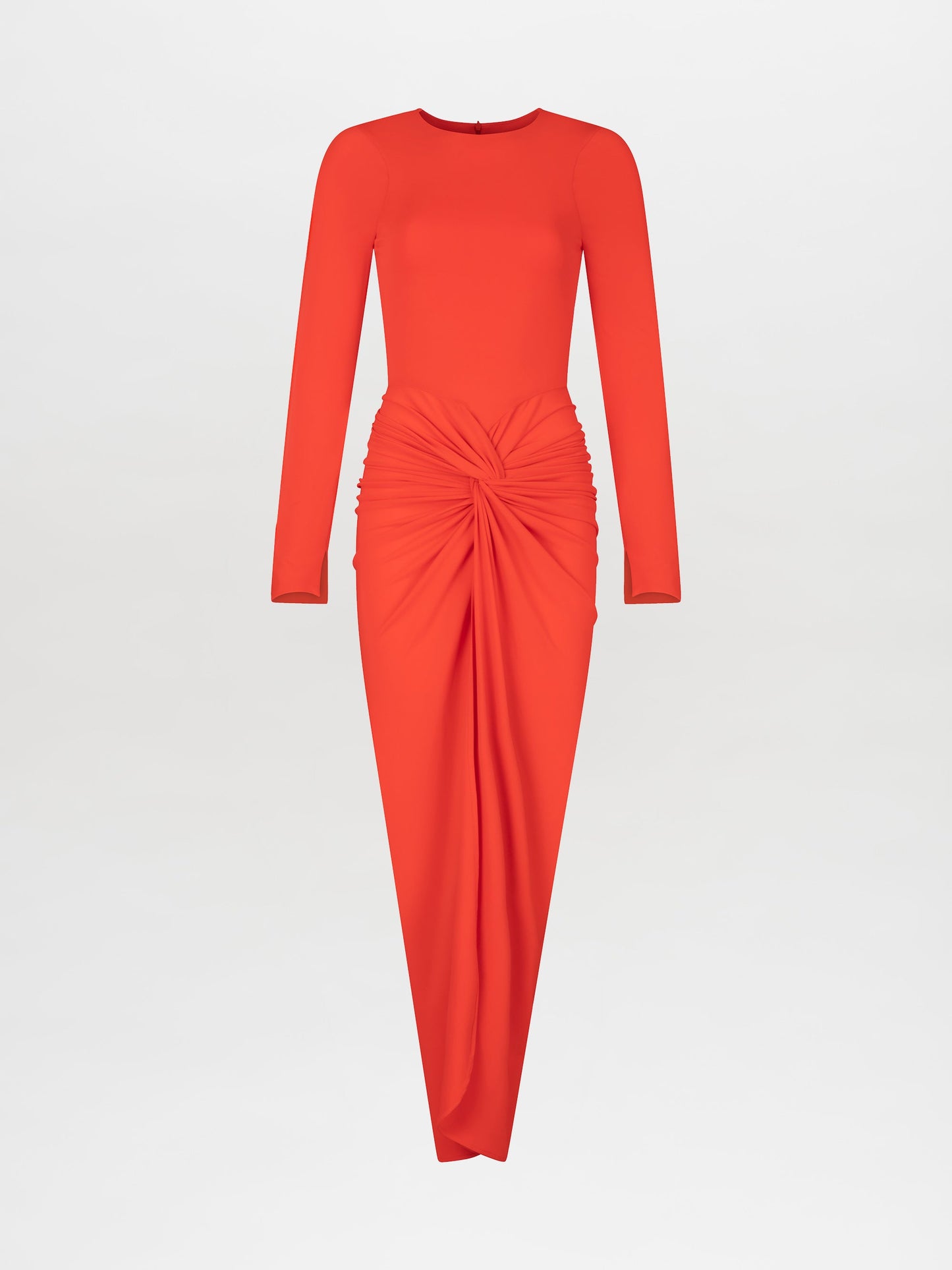 A person wearing the Sydelle Dress Tangerine, a long-sleeved orange dress featuring a knotted detail in the front, stands looking to the side. They are also donning sandals embellished with pearl-like beads. This elegant outfit will be available for pre-order and is anticipated to ship by 2025.