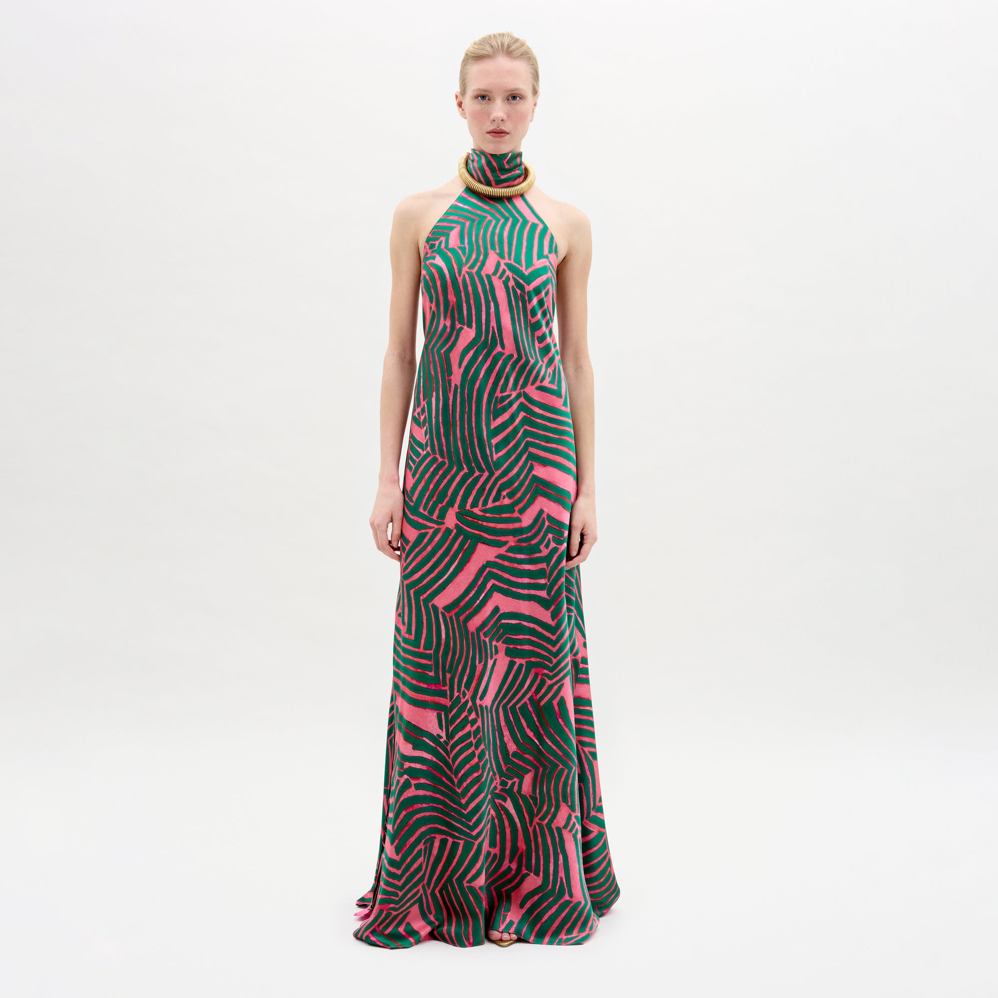 A woman wearing the Tila Dress in color Pink Green Abstract with a golden necklace on a white background.