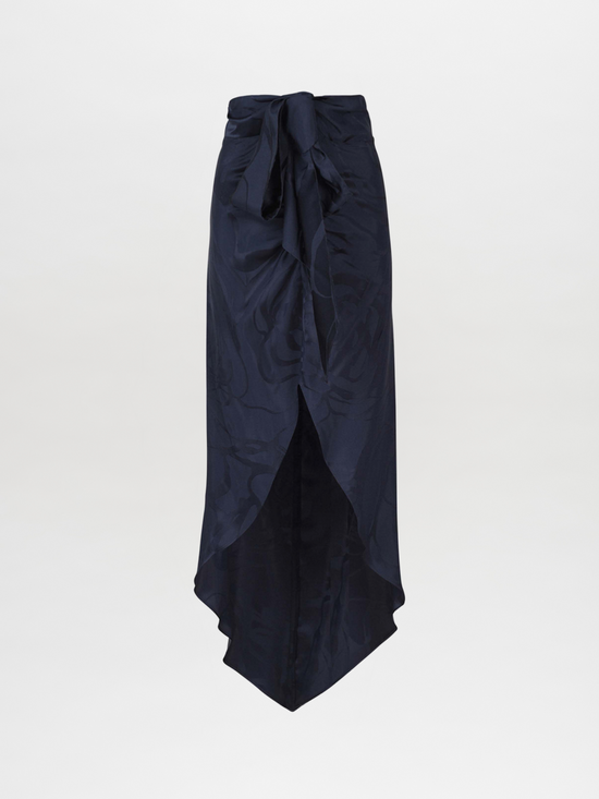 A Tara Skirt Navy Jacquard, featuring a tie at the waist and a mid-length navy floral jacquard design with an asymmetrical hemline, set against a plain white background.