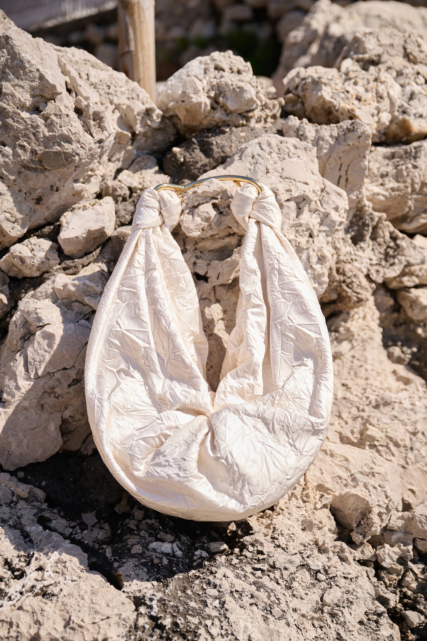 Sofia Bag off-white with gold handle on a rocky surface