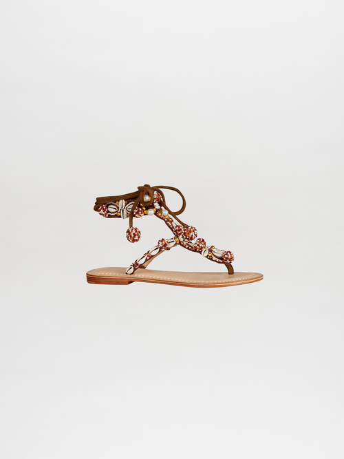 The Tisha Sandals, featuring a single sandal with brown straps adorned with colorful beads and decorations, is available for order and shipping, beautifully showcased against a plain white background.