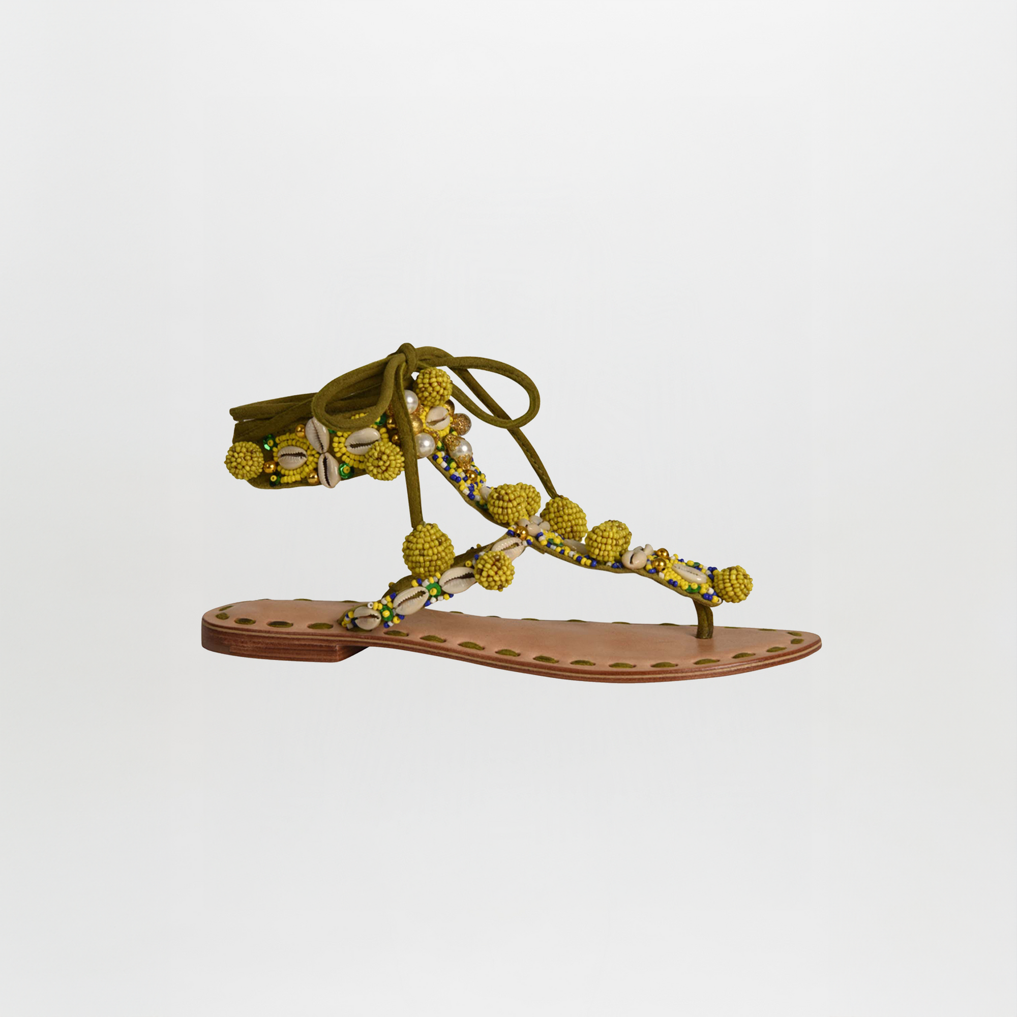 The Tisha Sandals Mustard feature a leather sole, olive-green lace-up straps, yellow pom-pom and bead embellishments, and decorative edge stitching.