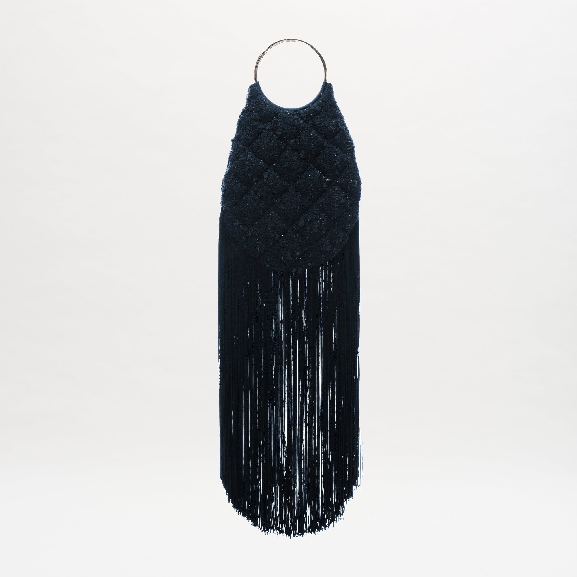 The Toblach Bag is a black, textured Jacquard bag featuring a quilted pattern, metallic top handles, and long black fringe at the bottom, shown against a white background.