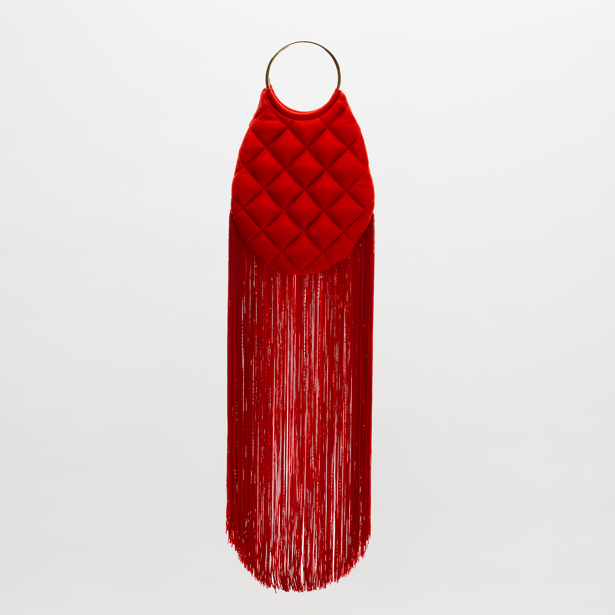 The Toblach Bag is a red quilted handbag made from Italian fabric, featuring metallic top handles and long red fringe along the bottom, displayed against a plain white background.