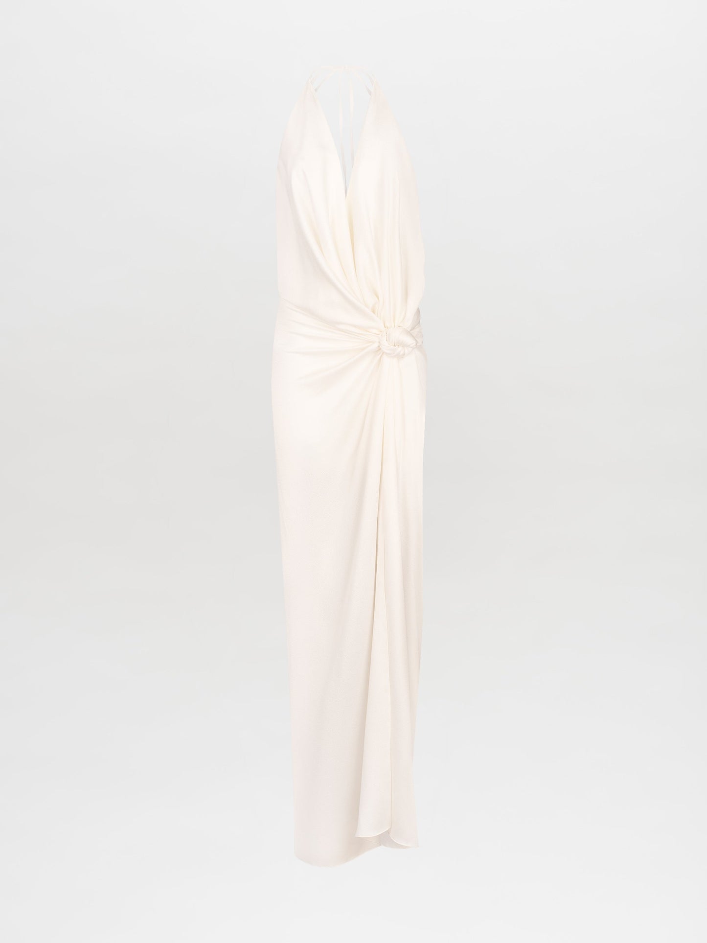 Person standing against a white background, wearing the Torgiano Dress White, which features a sleeveless halter design with a knot detail at the waist and a front slit. Pre-order now to ensure your dress is shipped by February 15th, 2025.