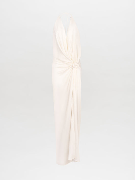 Person standing against a white background, wearing the Torgiano Dress White, which features a sleeveless halter design with a knot detail at the waist and a front slit. Pre-order now to ensure your dress is shipped by February 15th, 2025.