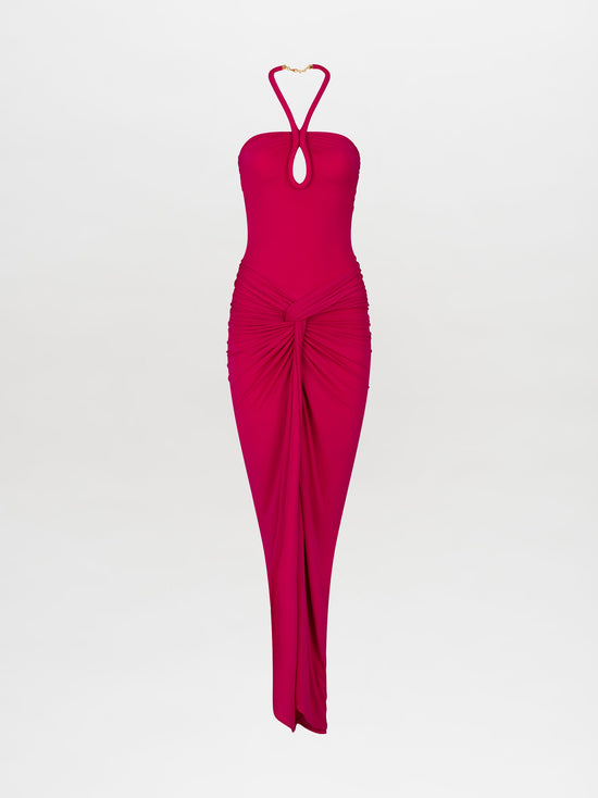 A woman stands in the Tori Dress Fuchsia, featuring a bright pink halter neck design with ruched detailing, paired with statement beige heels on a plain white background. This stylish ensemble is available for pre-order until February 15th, 2025.